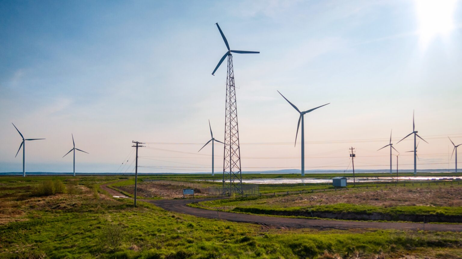 Wind turbines and a transmission tower in an open field at sunset