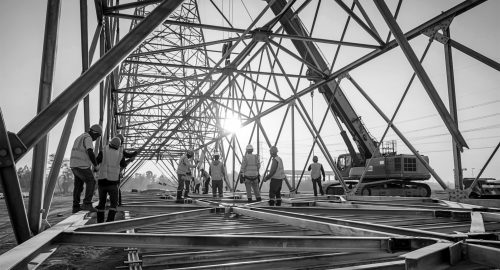Construction crew assembling metal framework components of elect