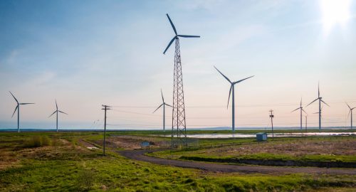 Wind turbines and a transmission tower in an open field at sunset